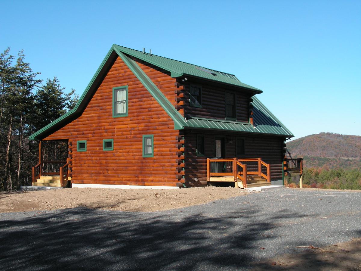 A log home with a green metal roof and a covered entry, gravel drive running up to it