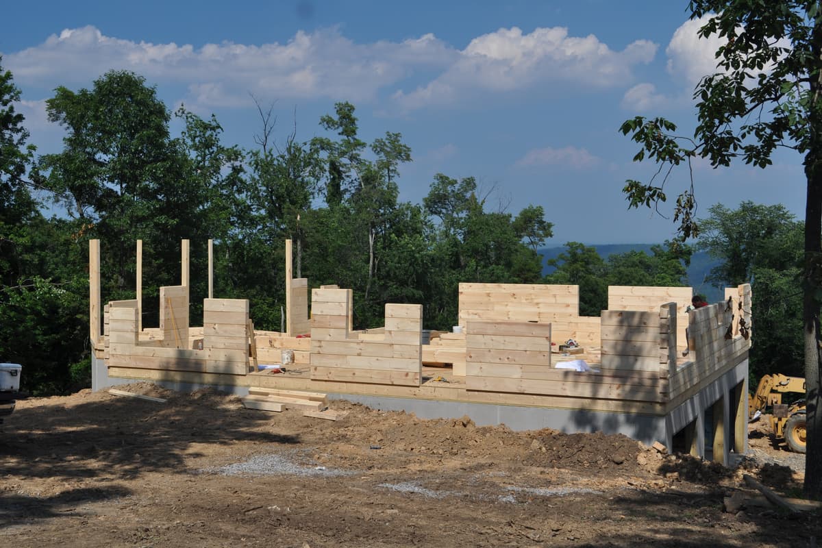 Log walls at window height with tall posts standing proud at the corners, the ridge visible past the opening.