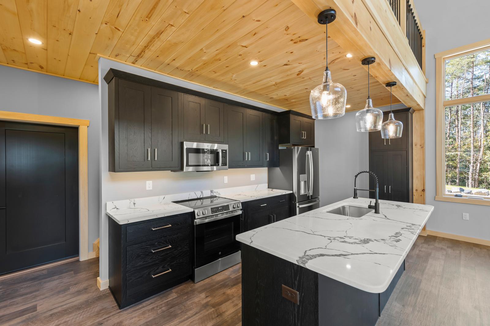 Kitchen with dark shaker cabinets, marble-look quartz island, pendant lights, and pine tongue-and-groove ceiling