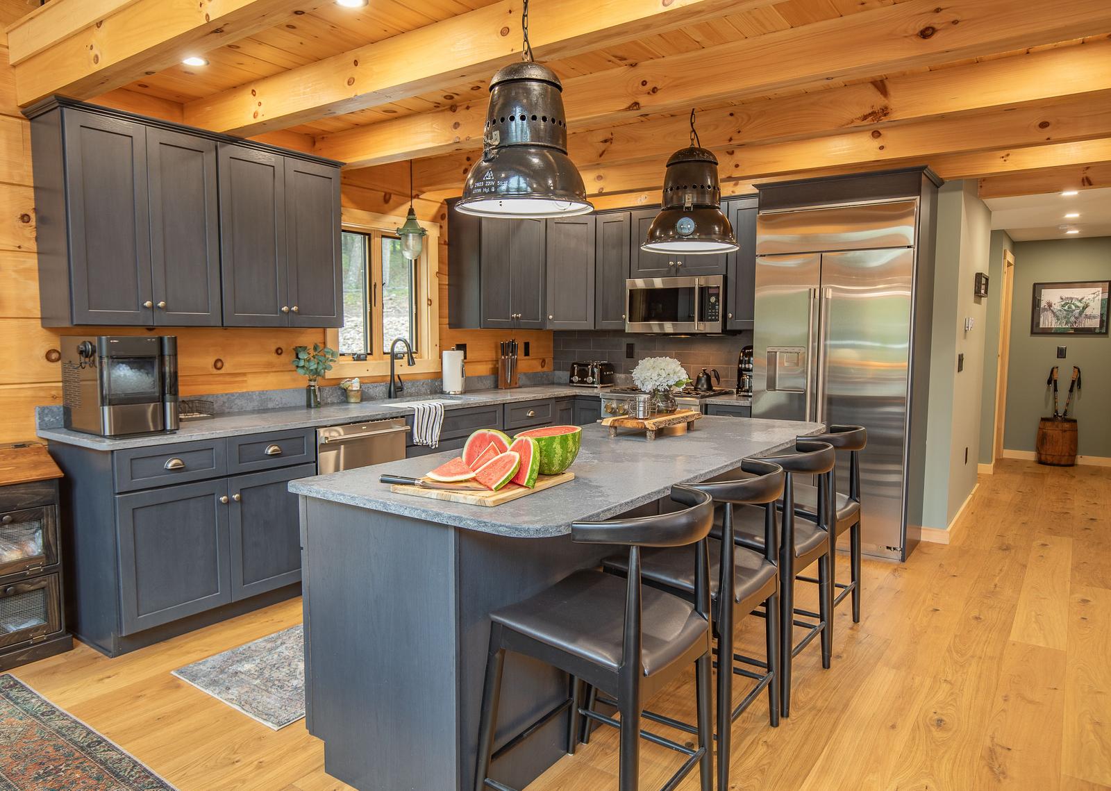 Kitchen with dark cabinets, granite countertops, pendant lighting, and exposed log walls