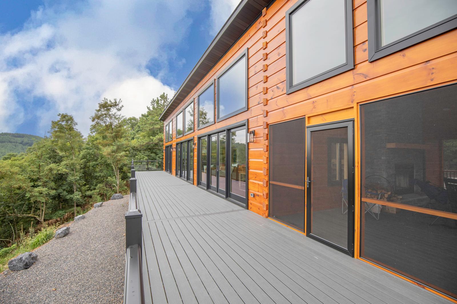 Long elevated deck running along the window wall of the home, with cable railing and a wooded hillside below