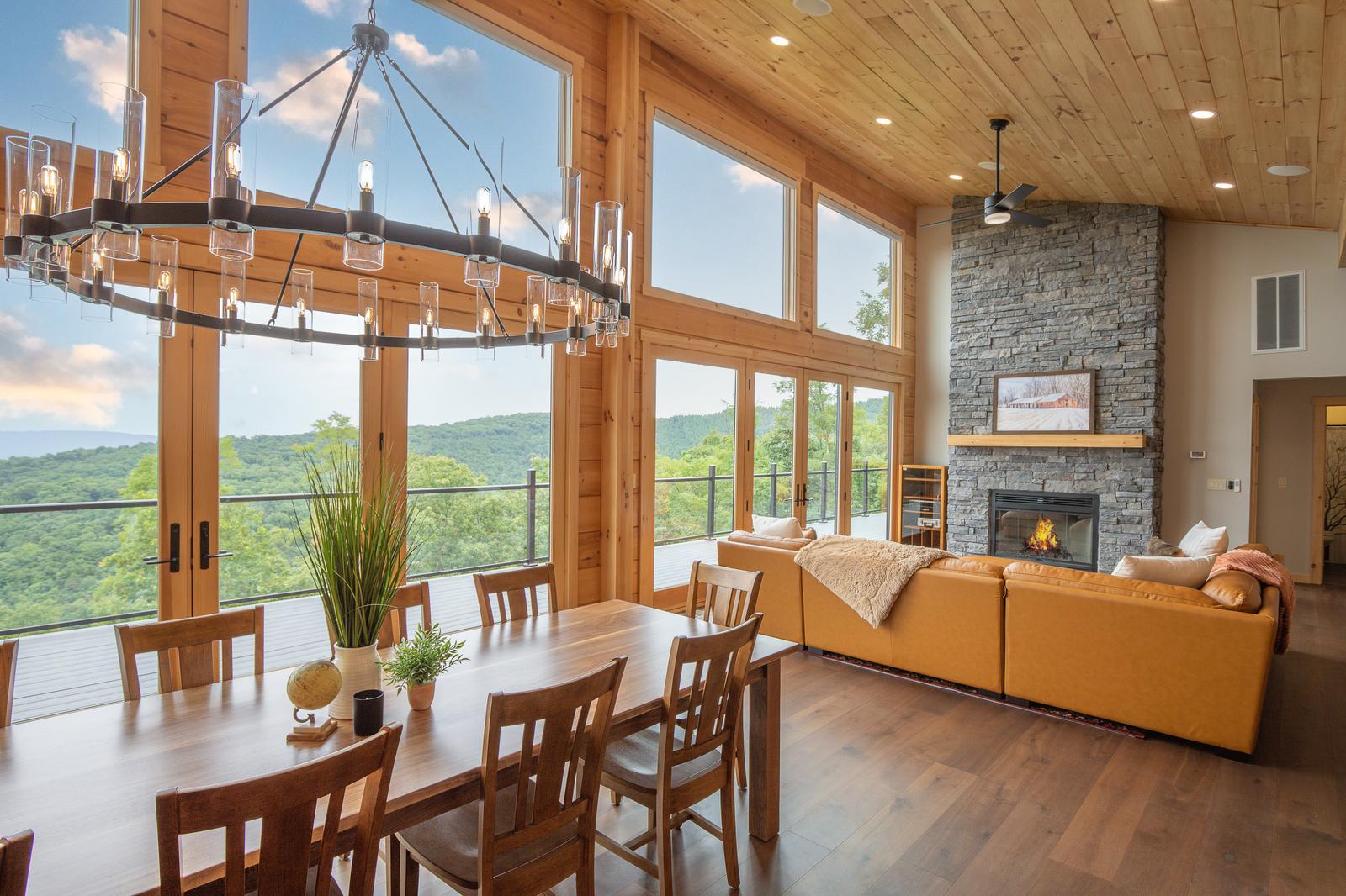 Closer view of the great room showing stone fireplace, floor-to-ceiling windows, and iron chandelier