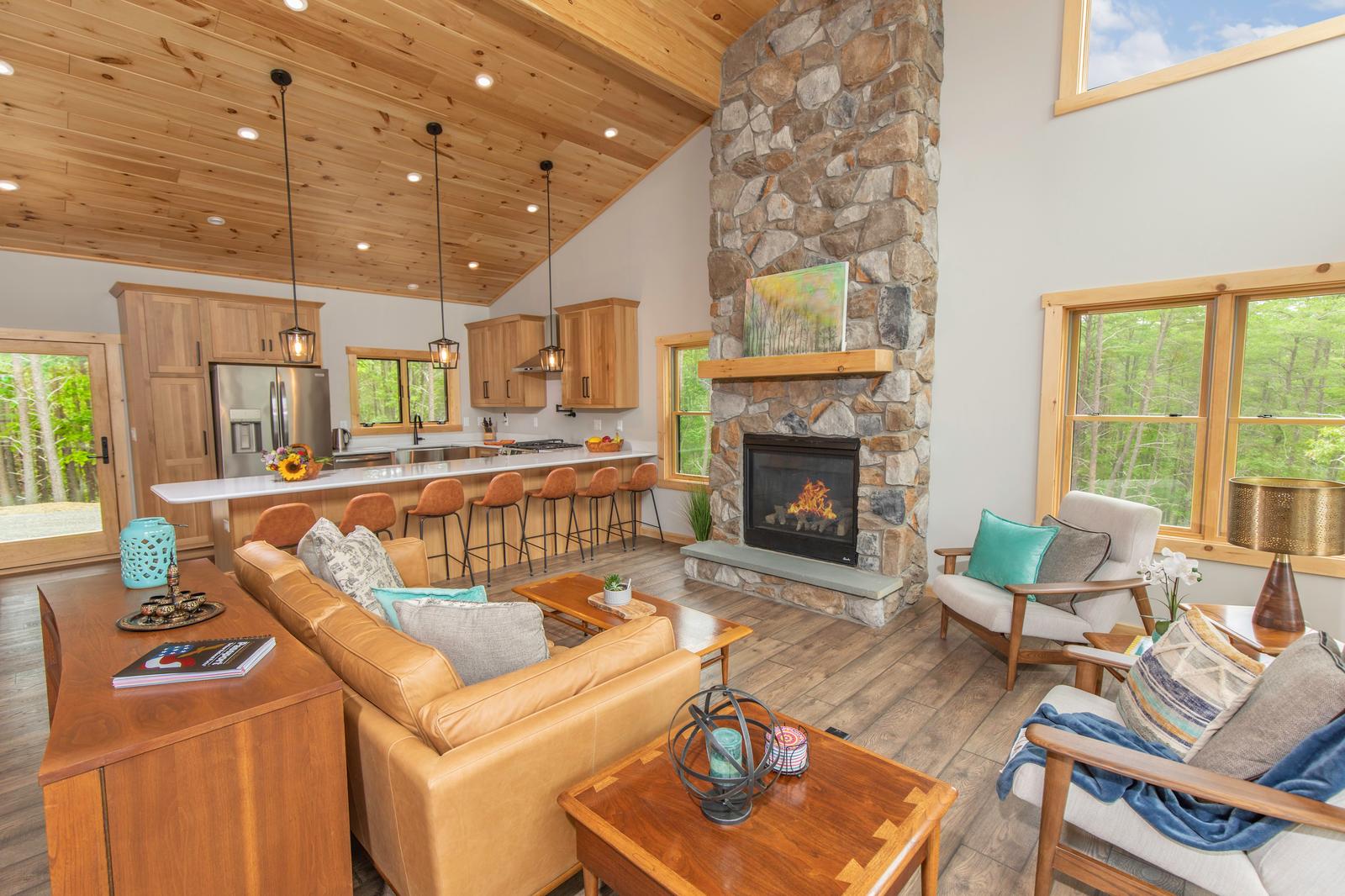 Open-concept great room with lit stone fireplace, pine vaulted ceiling, and kitchen island