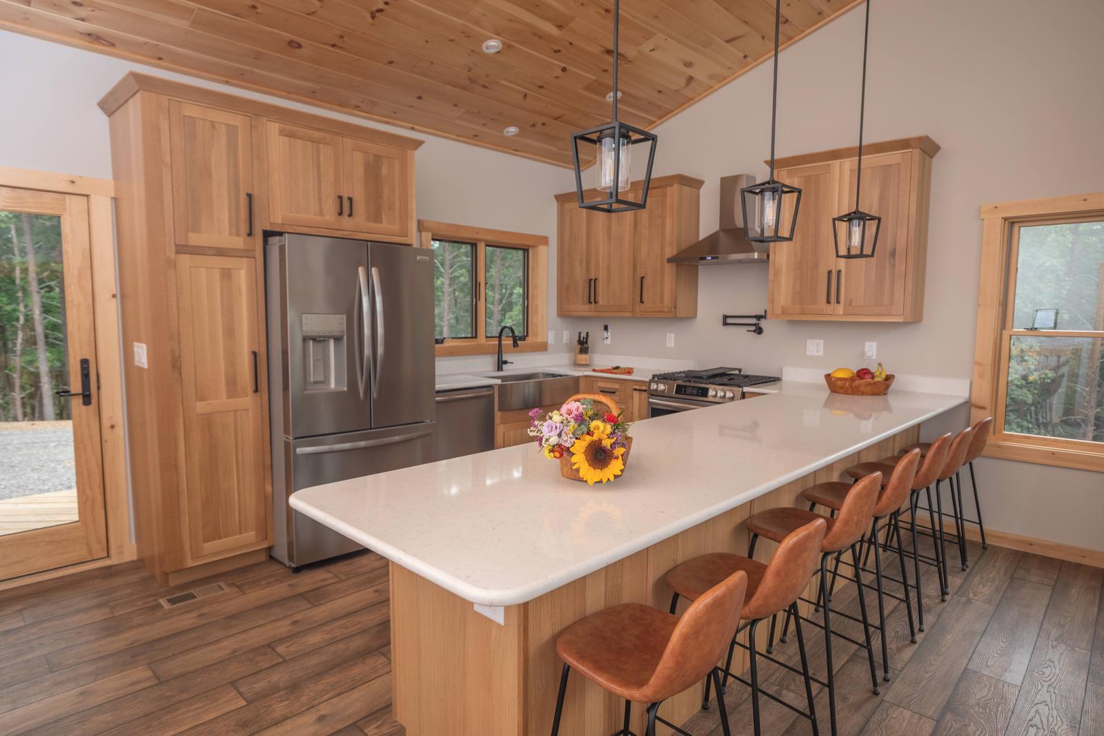 Kitchen with natural wood cabinets, white quartz island with bar seating, and stainless appliances
