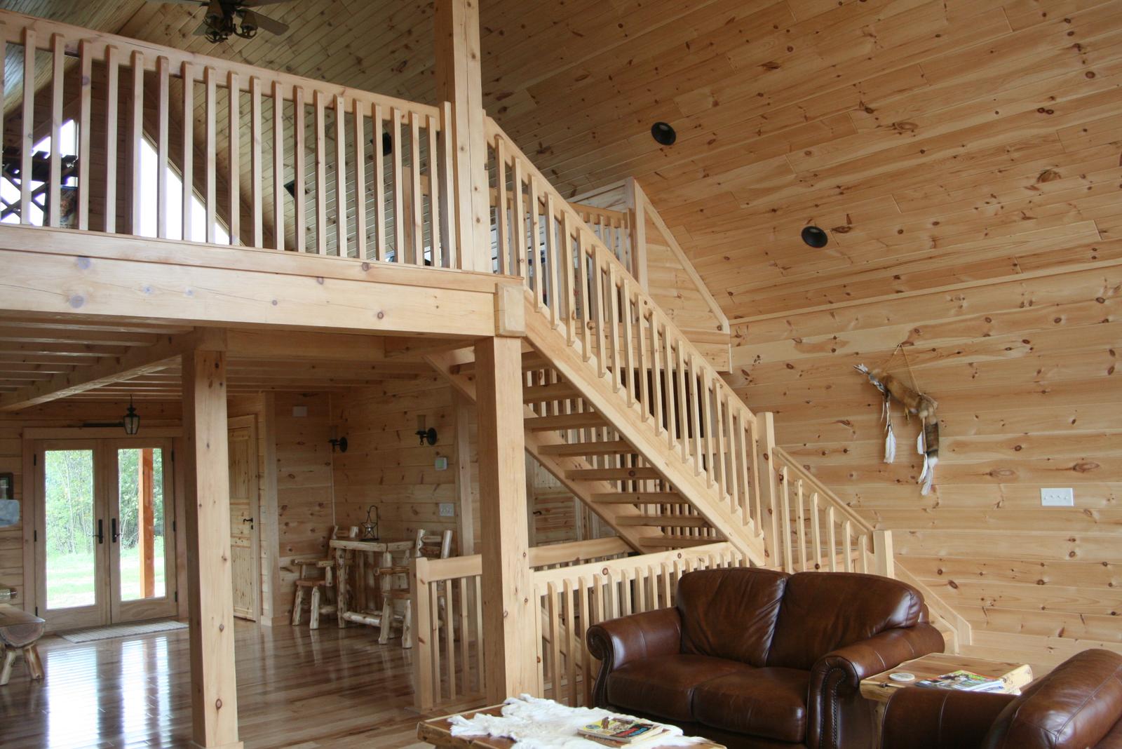 A staircase climbing to a loft that overlooks the great room, leather sofas below it and a vaulted board ceiling above