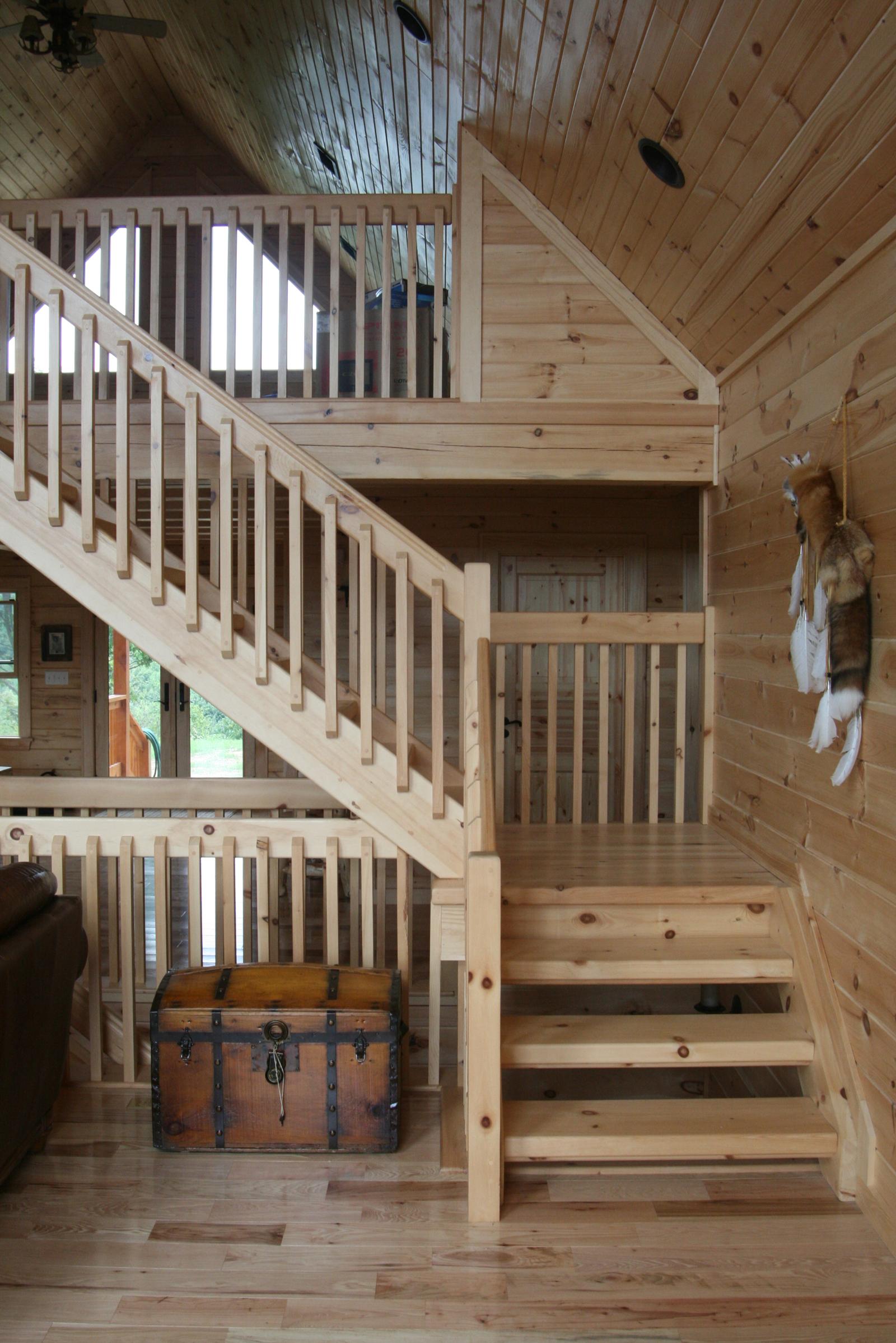 A stair turning at a landing beside an old steamer trunk, with a fur pelt hanging on the log wall