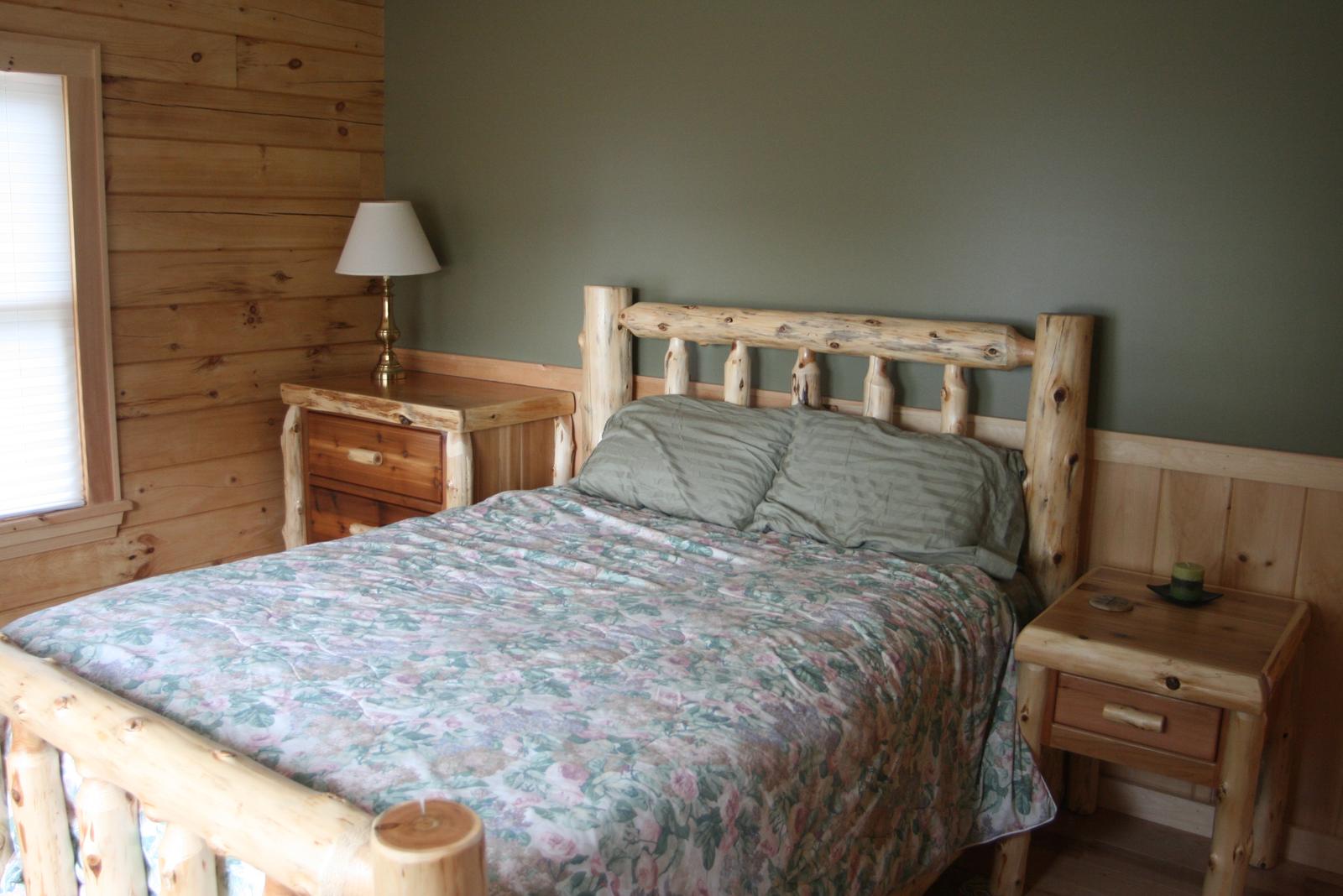A bedroom with a log bed and matching nightstands, one wall painted green above board wainscot and a log wall at the window