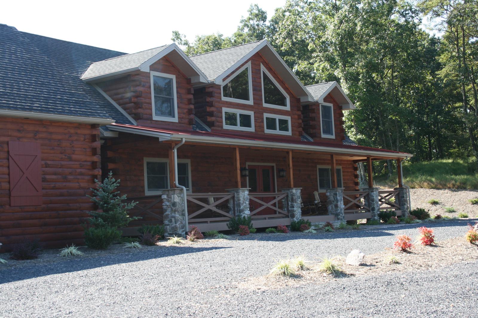 The front of a log home under a red porch roof, a prow gable of glass above the entry and rocking chairs on the porch