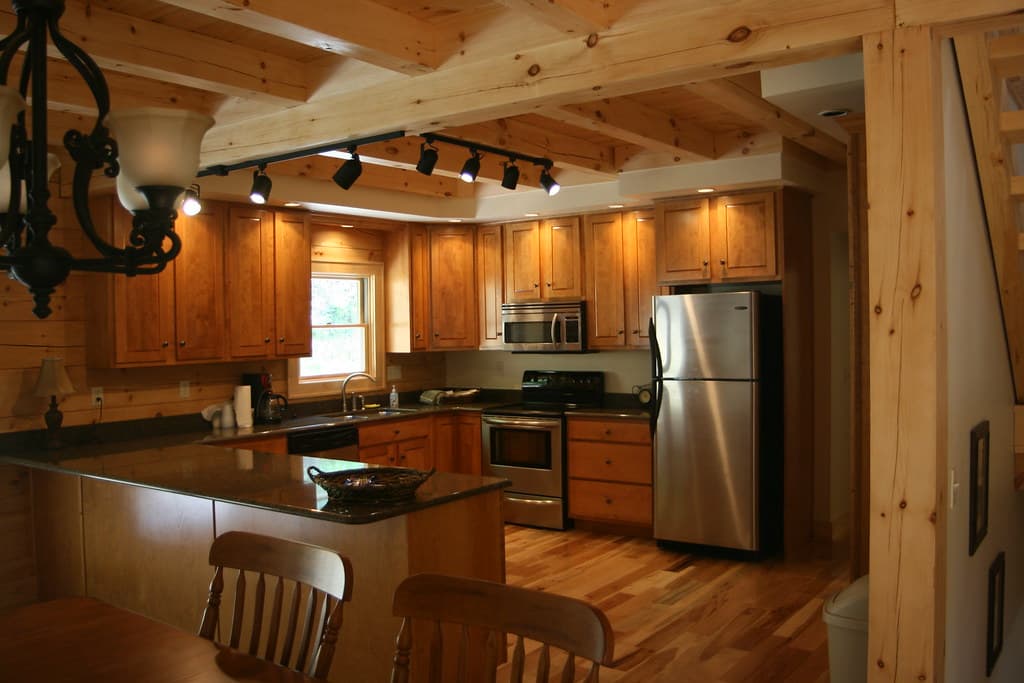 The main kitchen from the dining side, counter peninsula in front, track lighting under exposed beams
