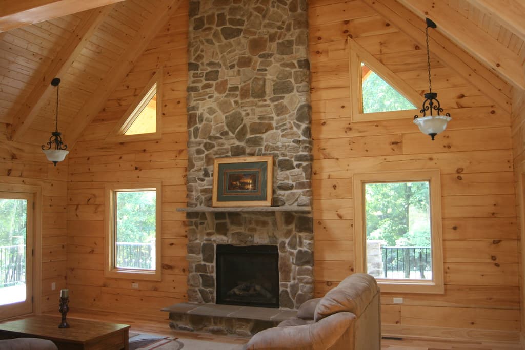 The great room, a stone chimney breast rising the full height between triangular gable windows, pendants hung either side