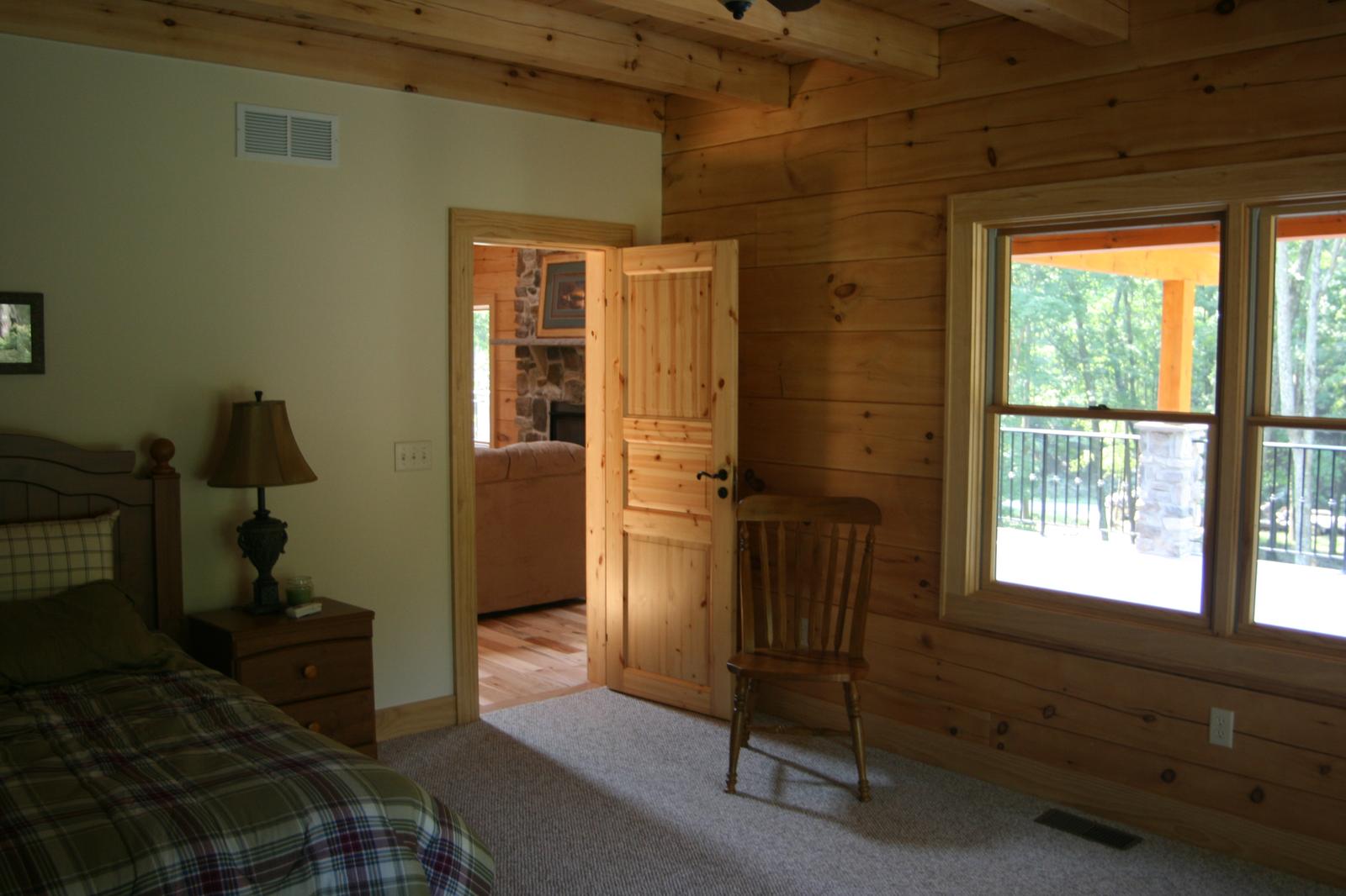 A bedroom doorway with board walls either side, a window looking out to the deck