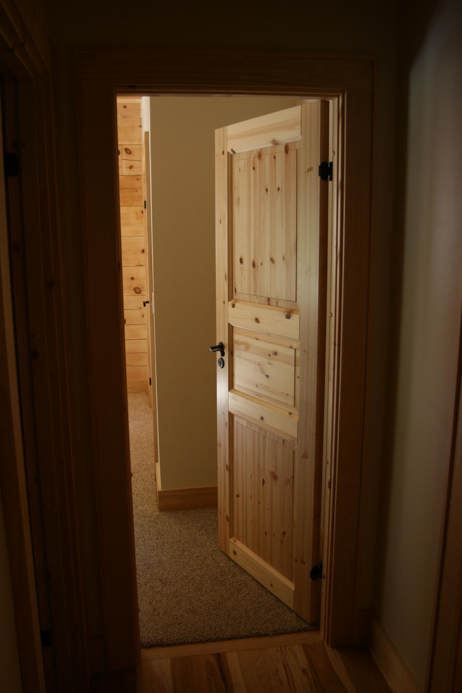 A paneled door standing open between two rooms, board walls and carpet beyond