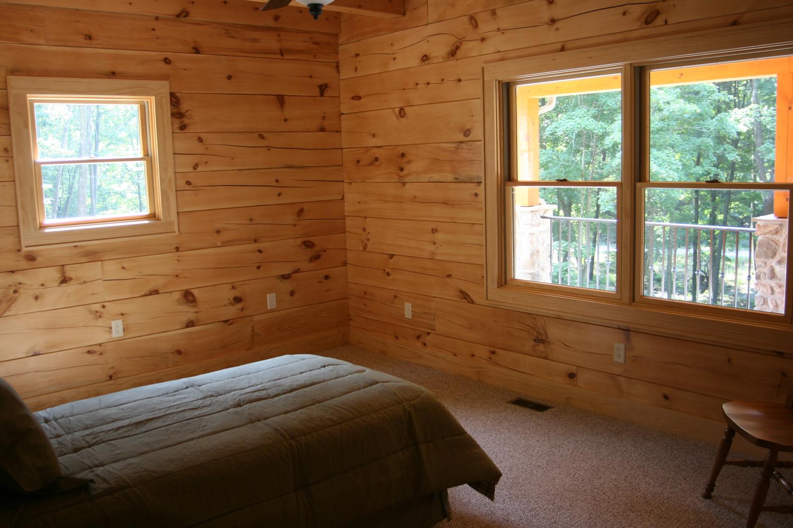 A bedroom with board walls and two windows, a bed low under the sill