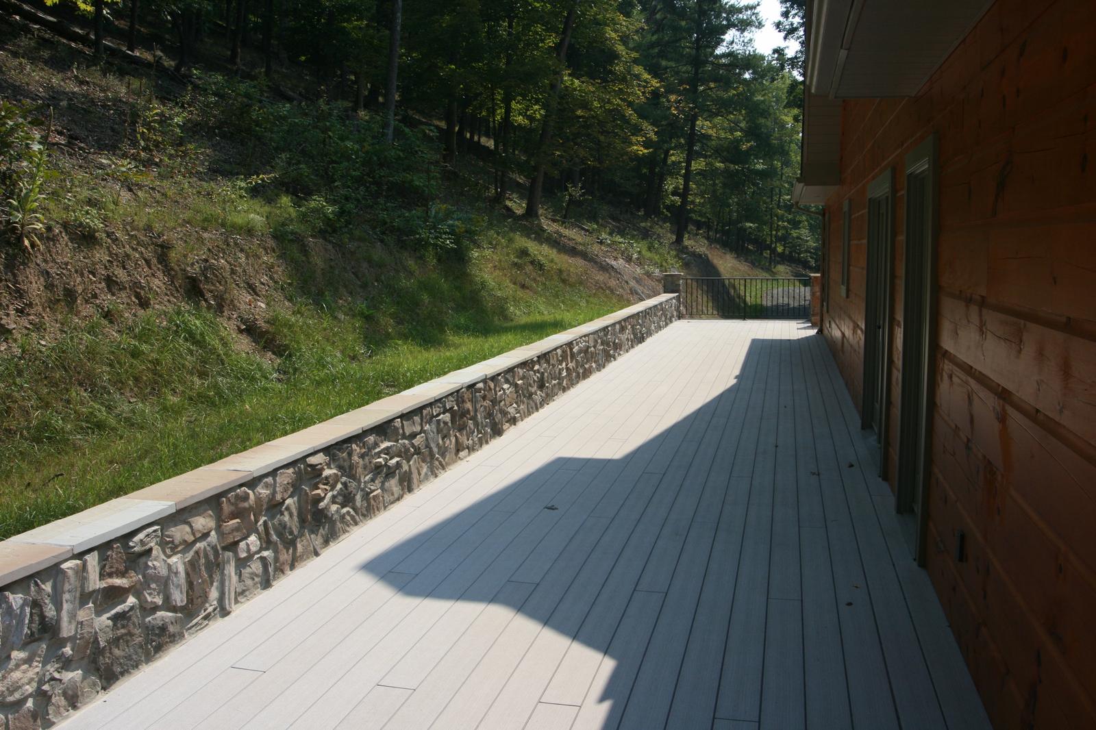 The deck along the back of the house, a stone retaining wall holding the bank behind it