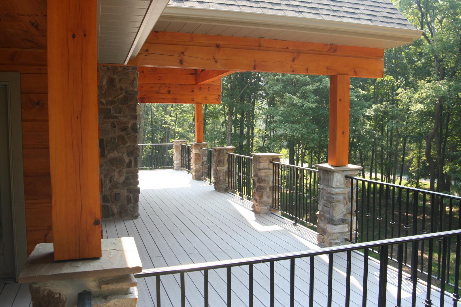 The porch along its length, timber posts on stone piers and railings running out to the trees