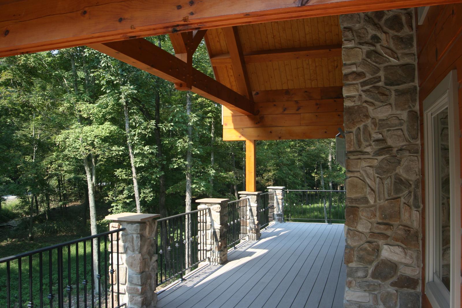 The porch turning a corner under its own gable roof, stone piers carrying timber posts