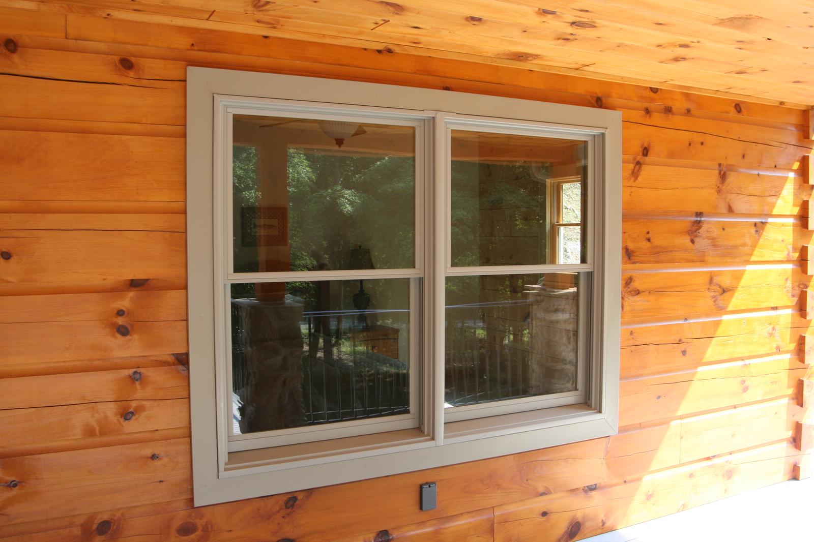 A sliding window set into a log wall, the porch reflected in the glass