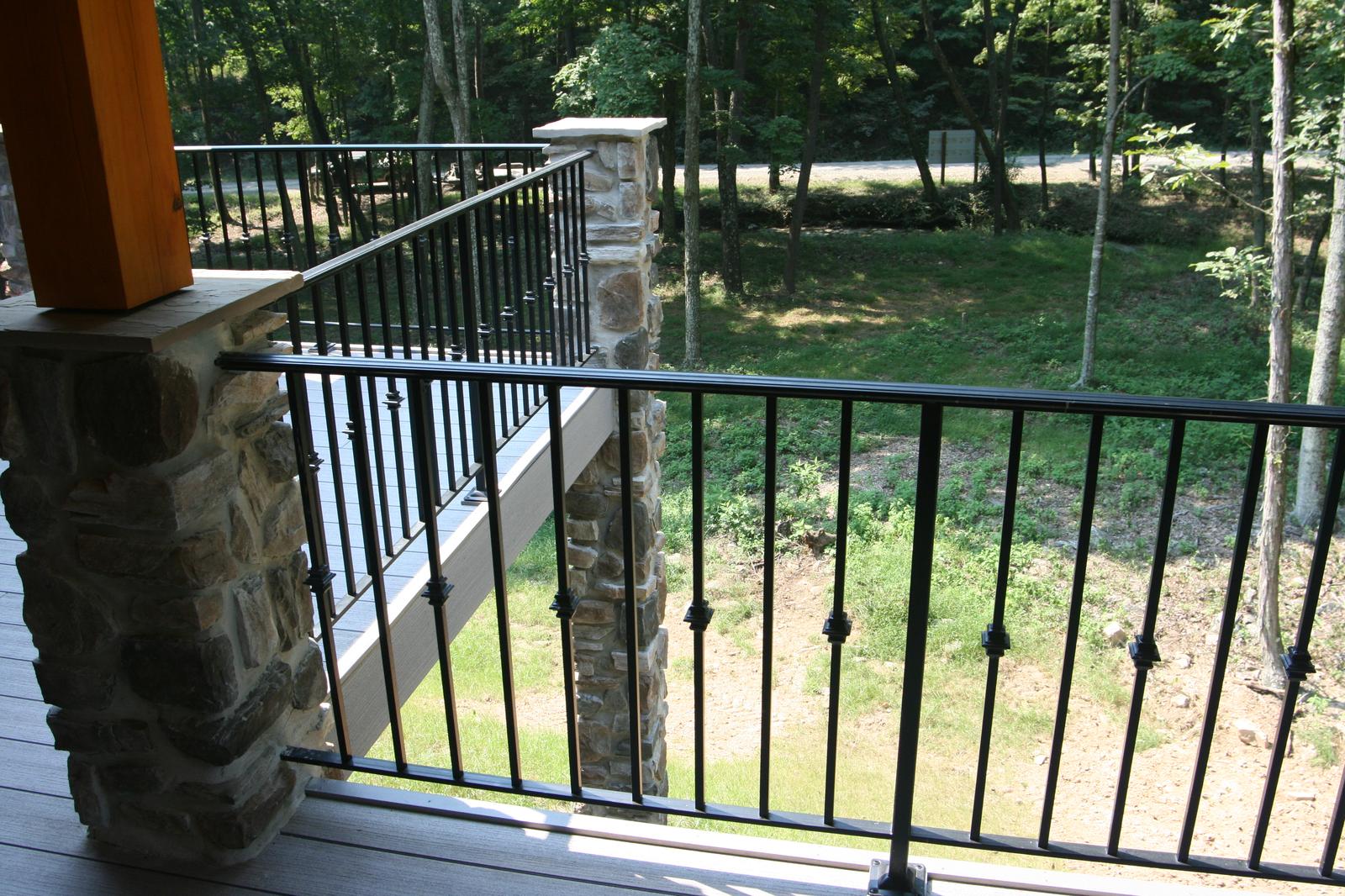 The porch railing and a stone pier close to, mown ground and a drive beyond