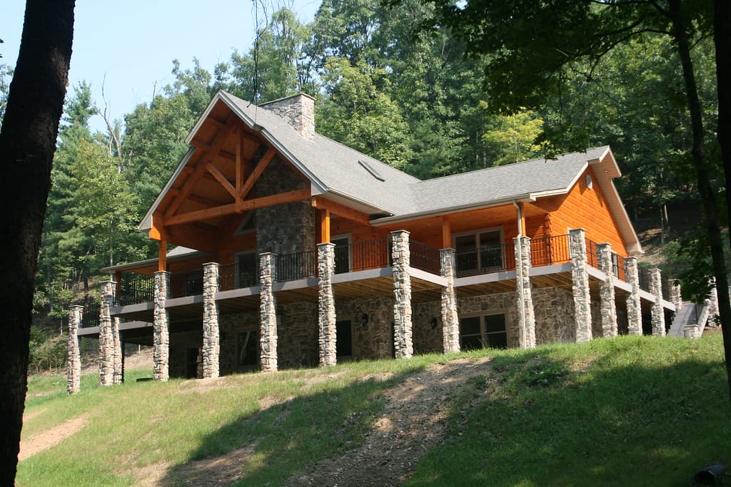 The house from below across the slope, its deck carried on stone piers, timber truss filling the entry gable