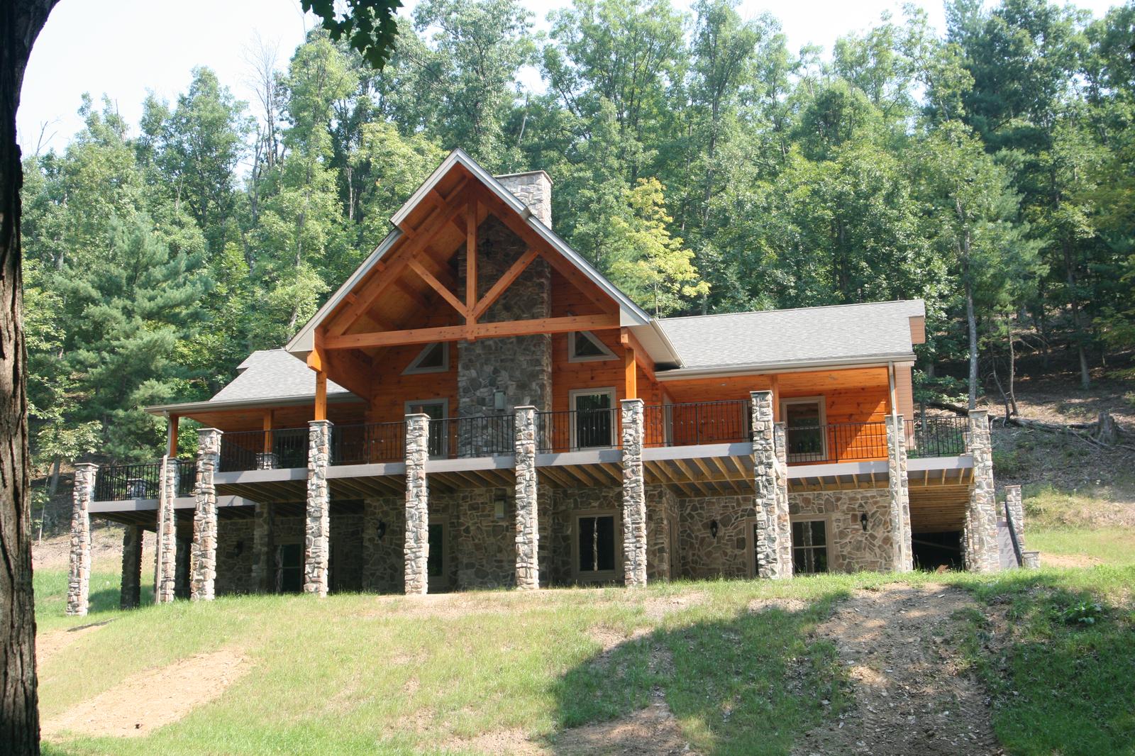 The home from across a mown clearing, a heavy timber truss in the entry gable above a porch on stone piers