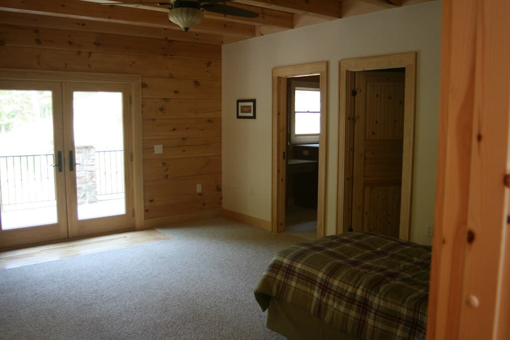 A bedroom with glazed doors onto the deck, a doorway through to the bath, corner of the bed in the foreground