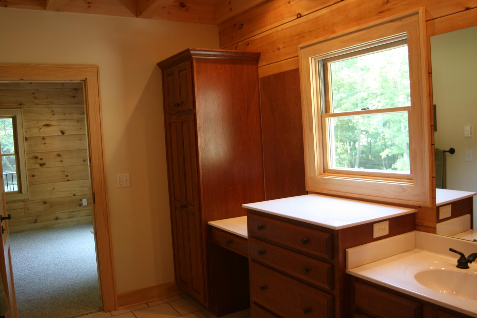 The same bathroom from the other side, a tall cabinet beside the basin and a door standing open