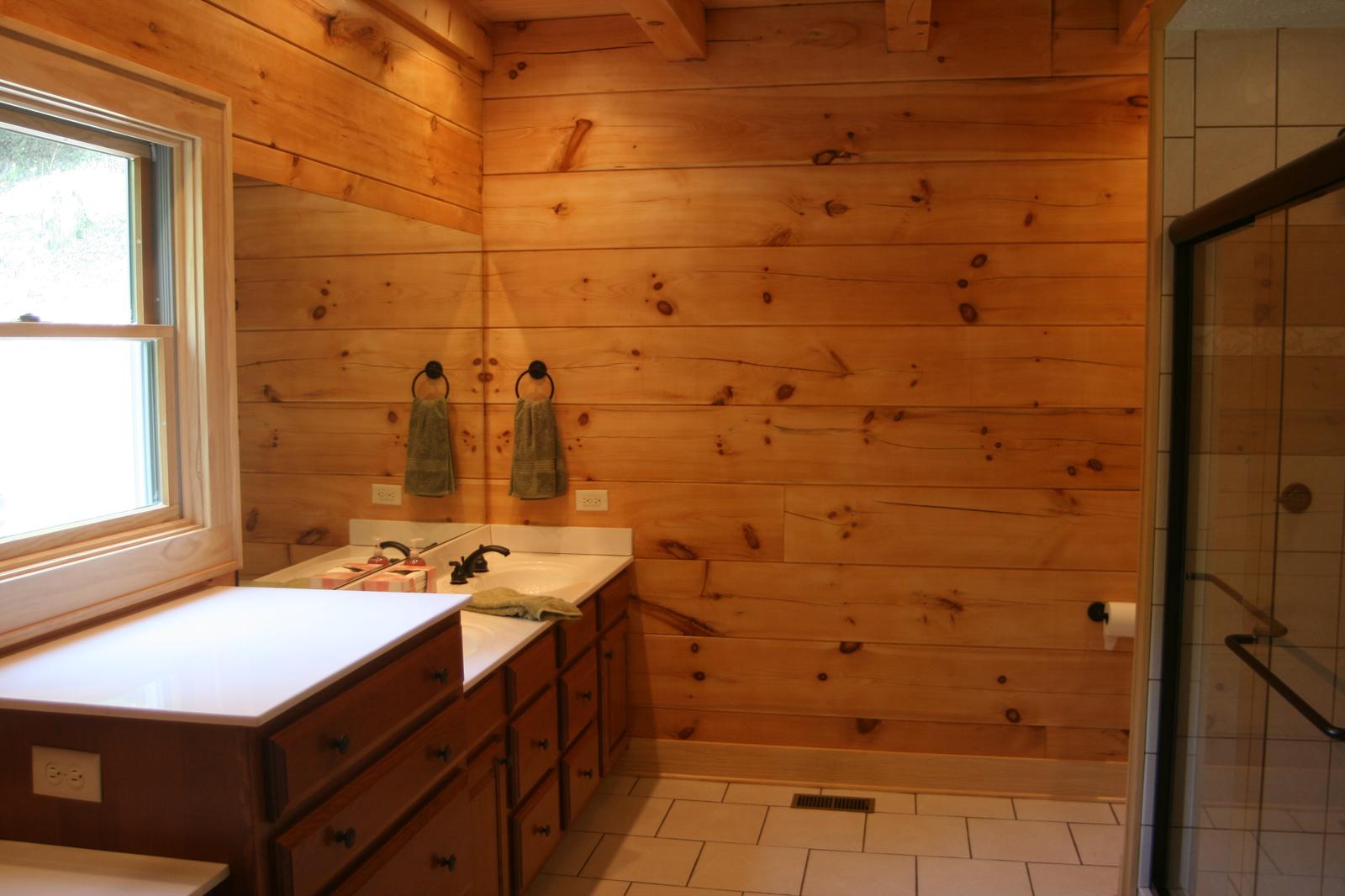 A bathroom vanity under a window, a tiled floor and a glass shower door at the end