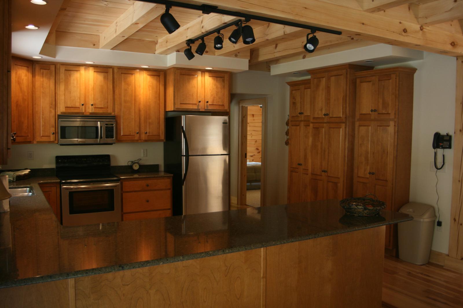 A kitchen with wood cabinets and a stainless range and refrigerator, exposed beams and track lighting overhead