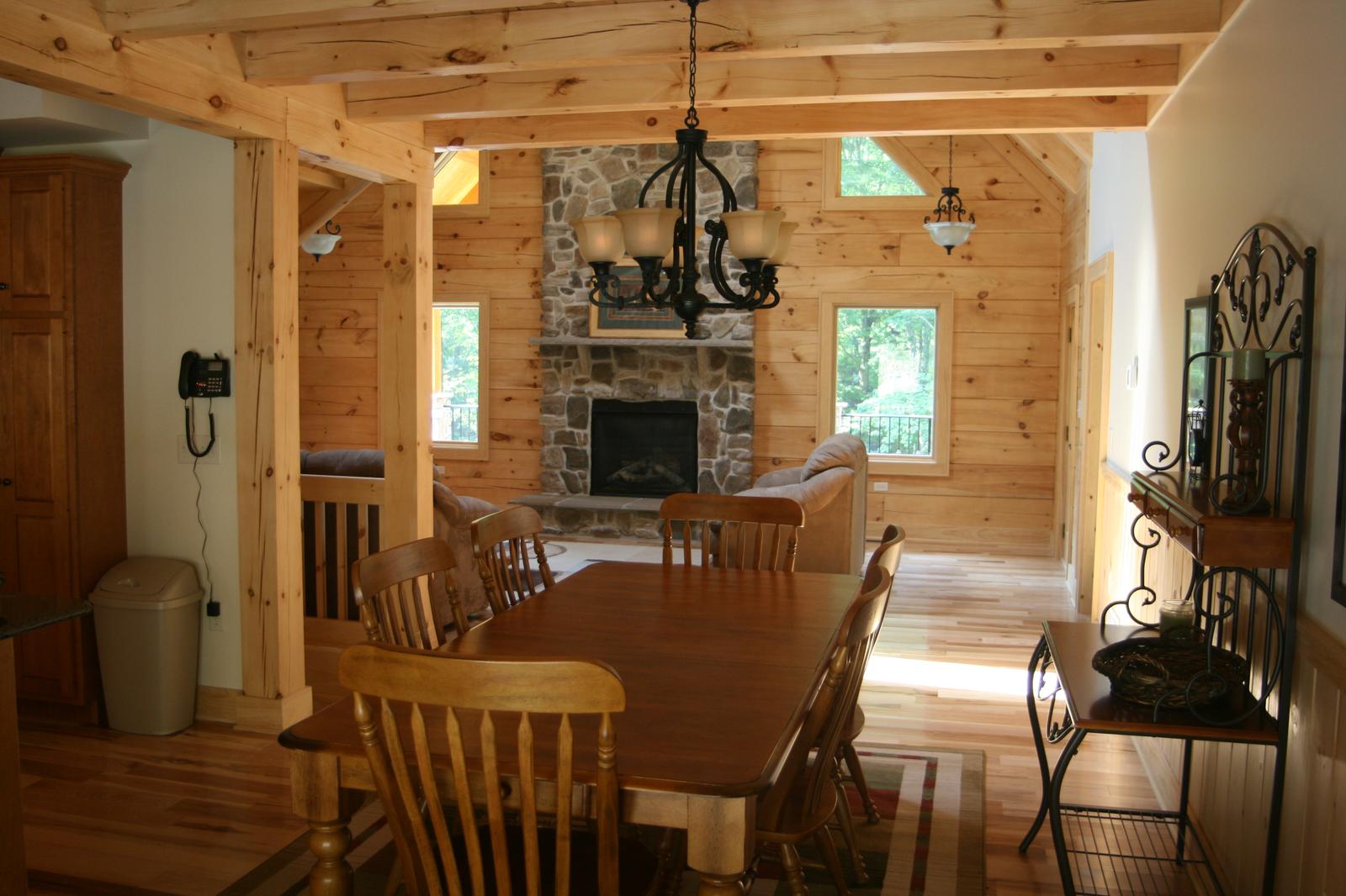 A dining table under a chandelier, the great room and its stone fireplace visible past the opening