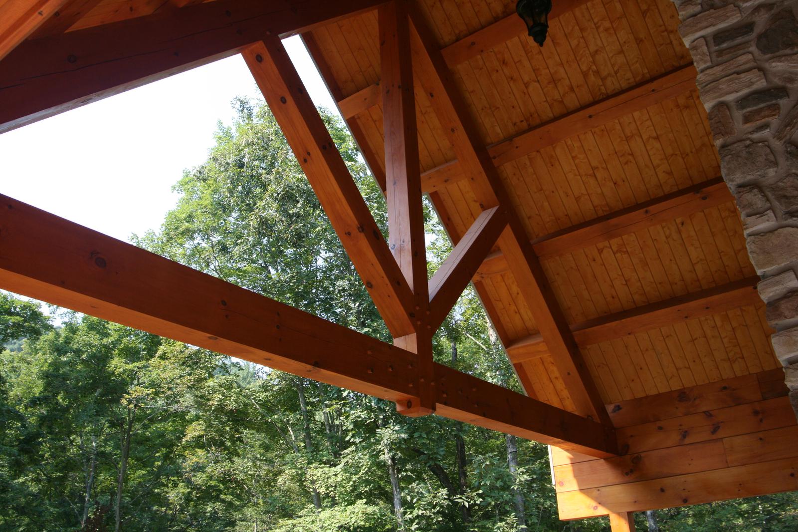 The underside of the porch gable, exposed timber truss and rafters against a board ceiling
