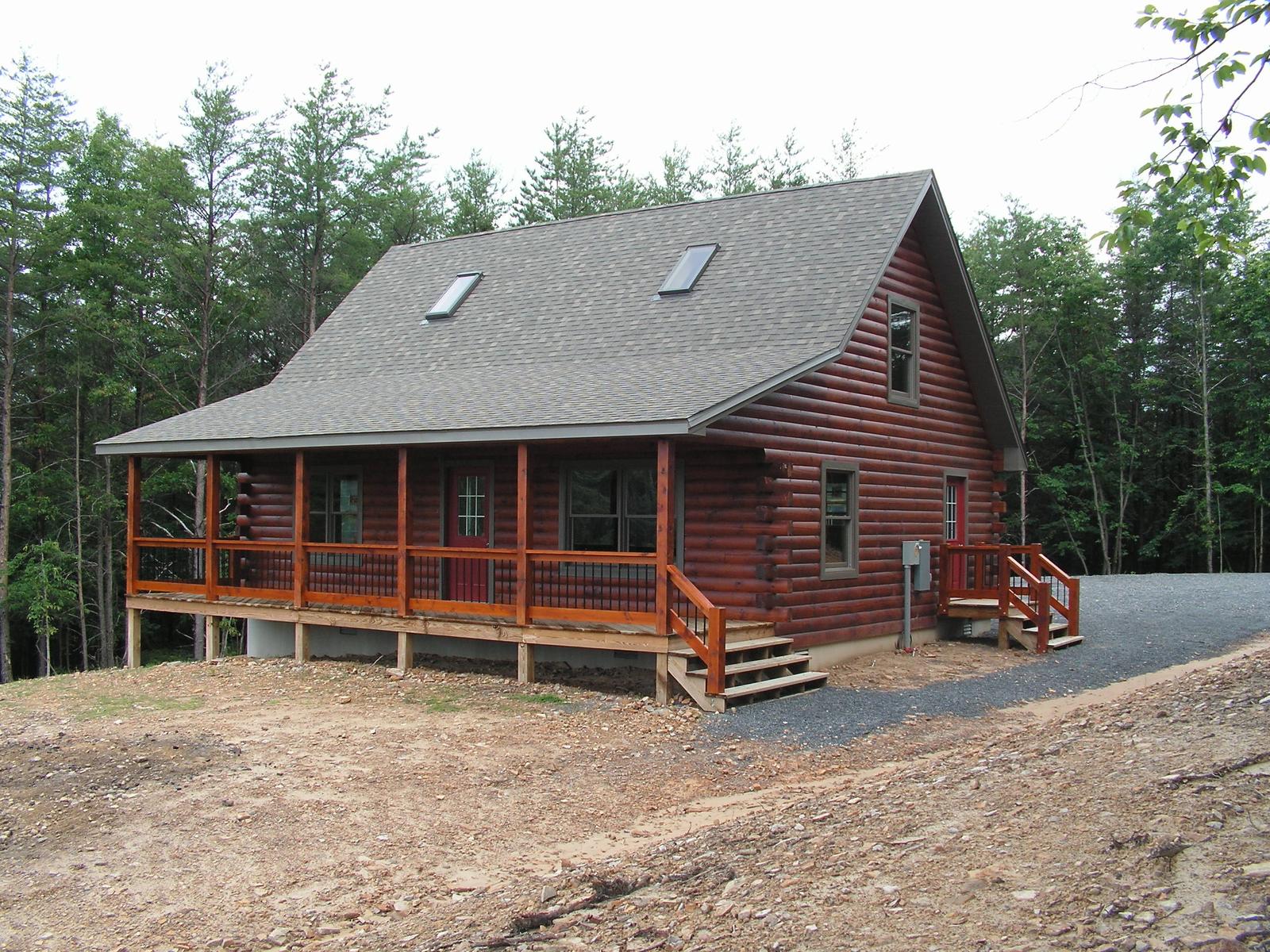 A log home with a full-length covered porch, roof skylights above and a gravel drive curving to the steps