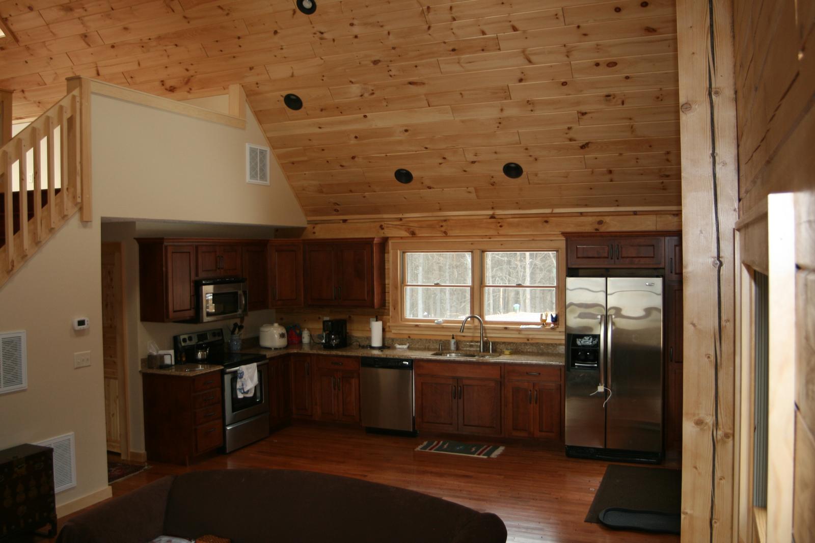 A kitchen under a sloped board ceiling, dark cabinets and stainless appliances along two walls