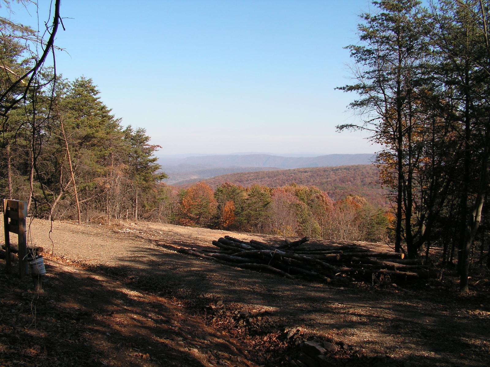 A graded clearing on a ridge with cut logs stacked at its edge and a timber marker frame in the foreground, fall woods falling away below