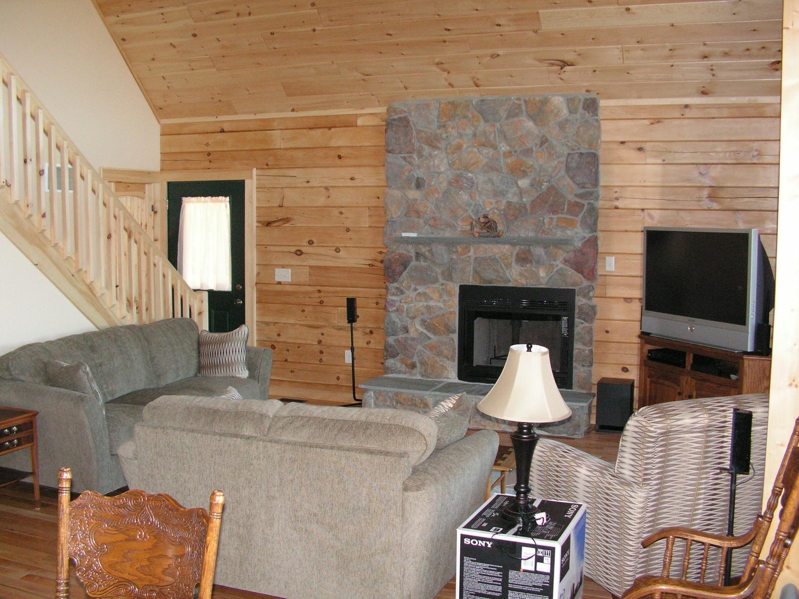 A living room with a stone fireplace between board walls, seating drawn up around it