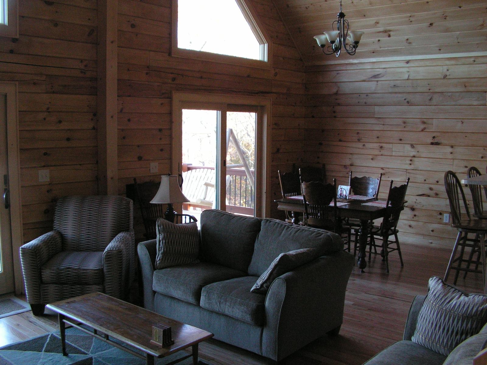 The room from the far end, a table and chairs by the window and a glazed door to the deck