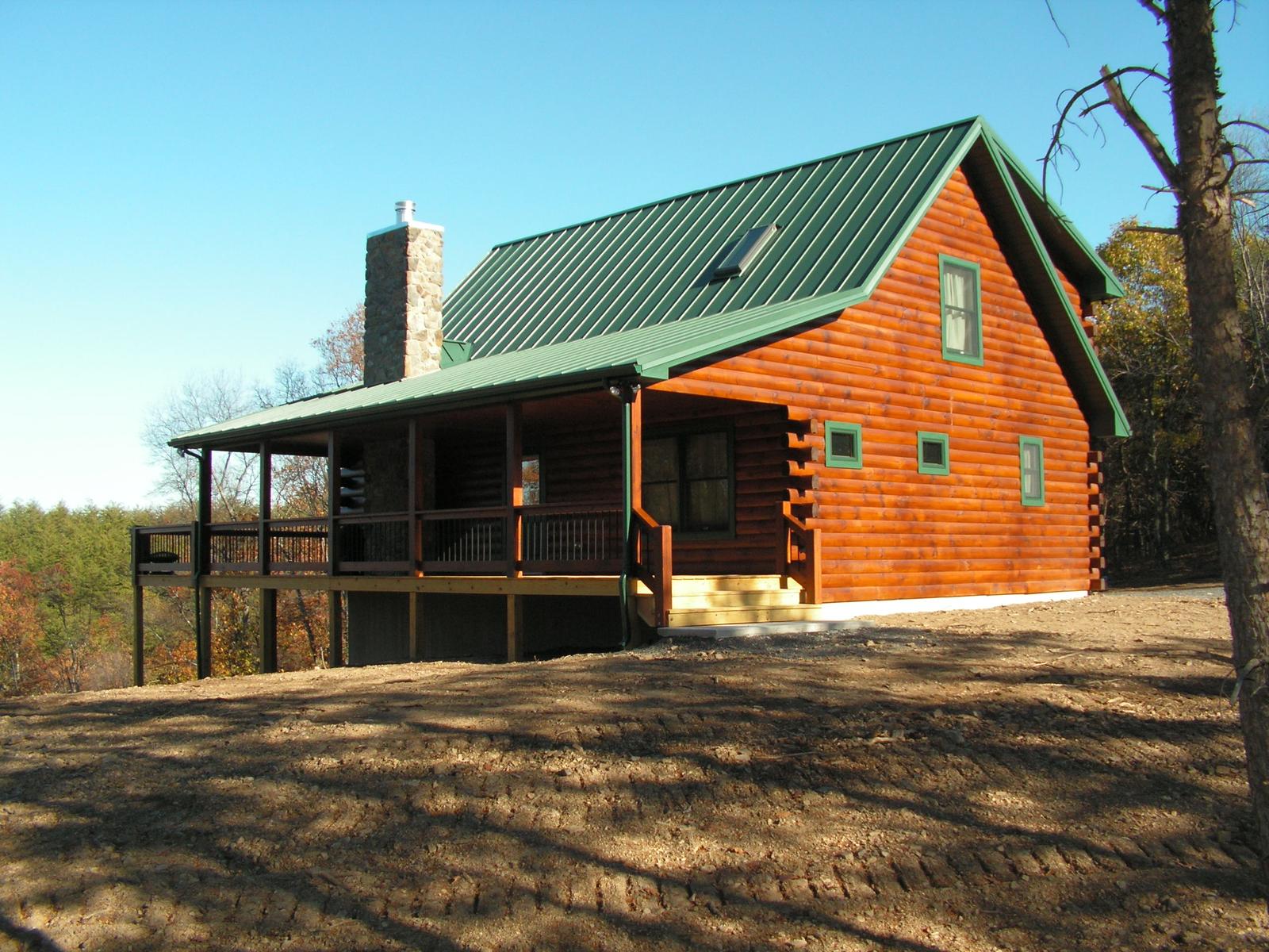 The home from the open side, a stone chimney at the gable and a covered porch below