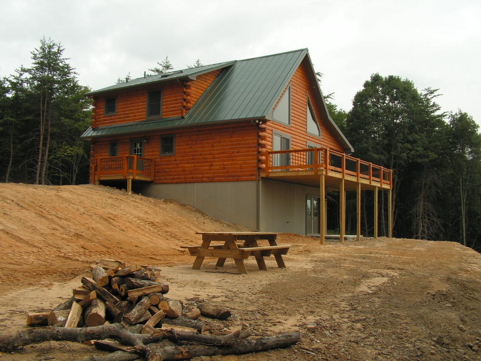 The home from below the bank, a picnic table and cut logs in the foreground