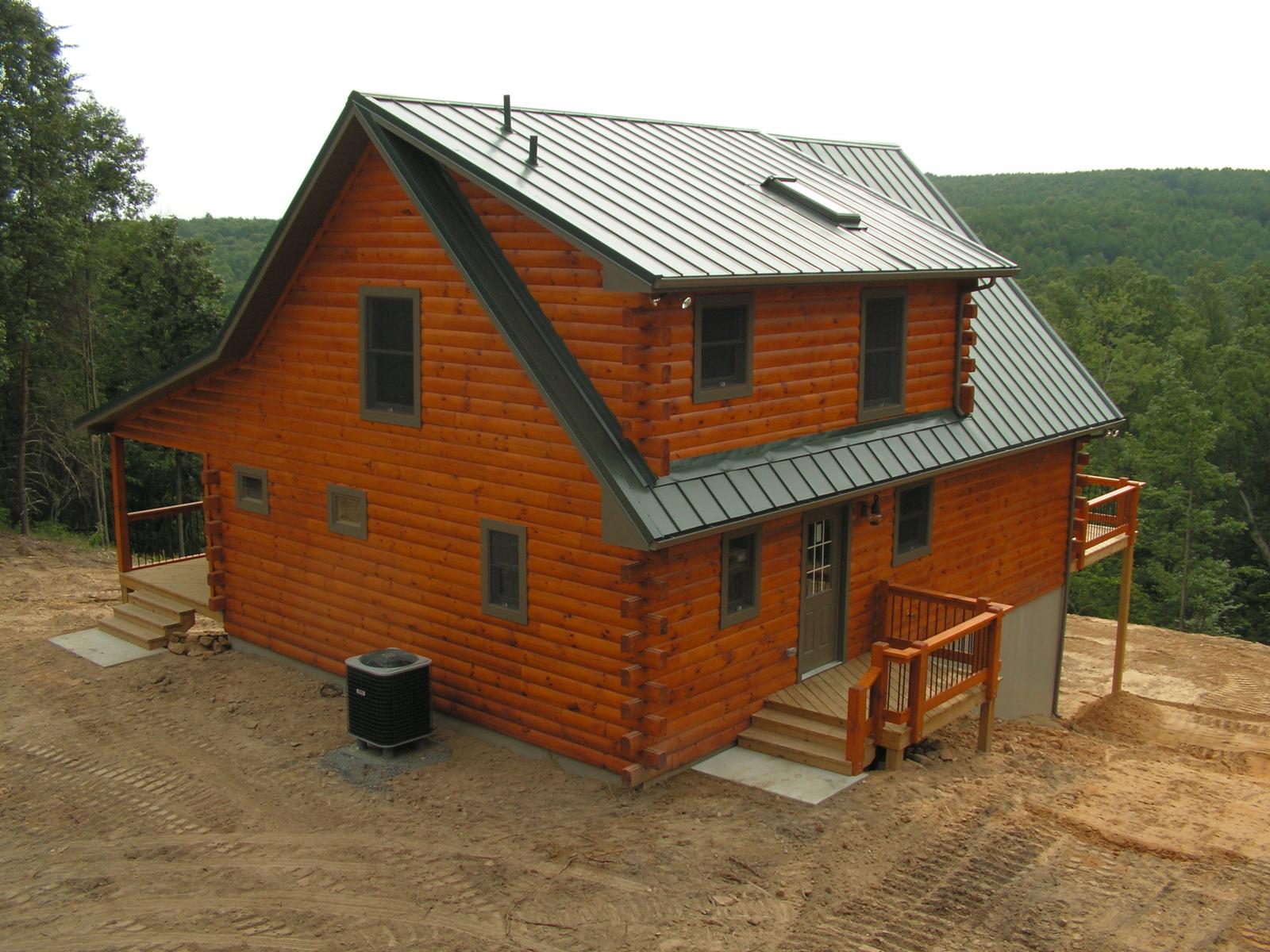 A log home with a green metal roof on freshly graded ground, entry steps at the near corner