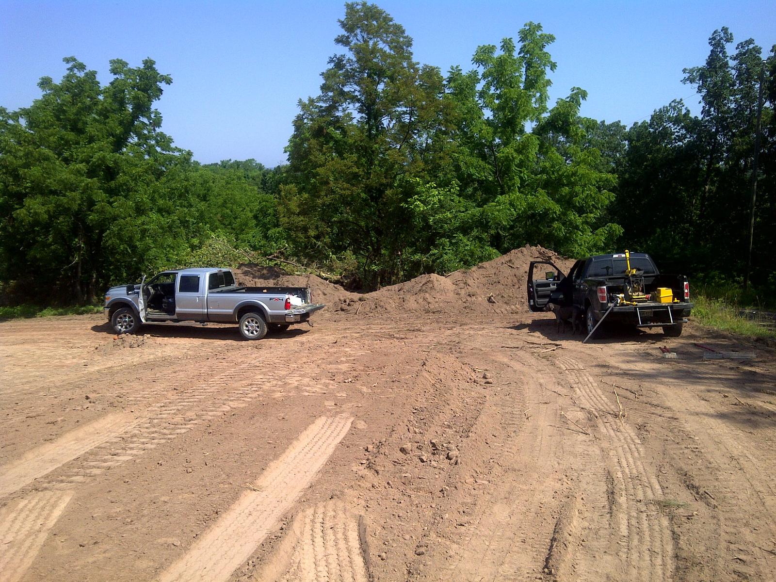 Two pickups parked on bare graded ground beside a mound of earth, one carrying equipment in the bed