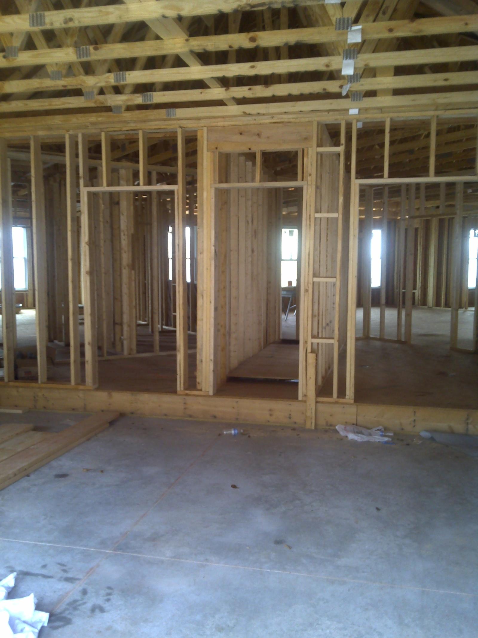 The interior in stud framing, ceiling joists overhead and door openings running through to daylight at the far wall