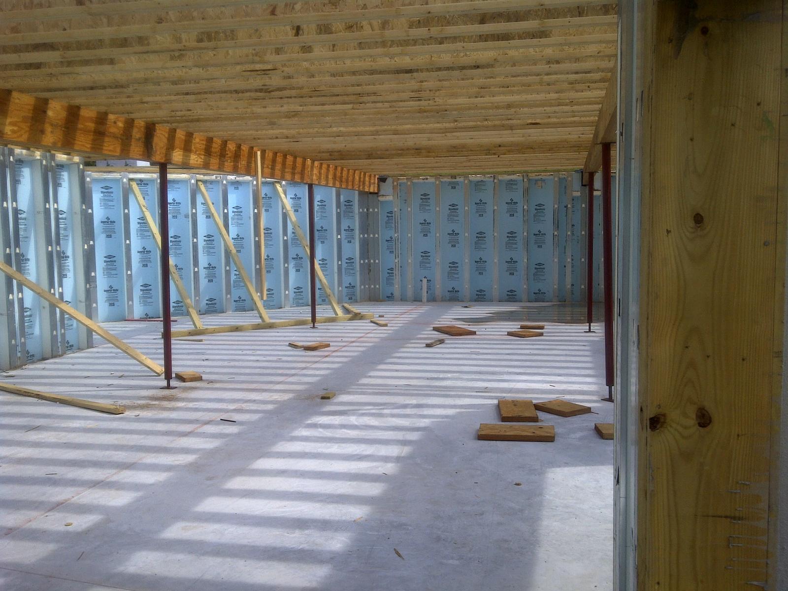 The basement toward a corner, insulated panels and braced framing beneath the joists and subfloor above