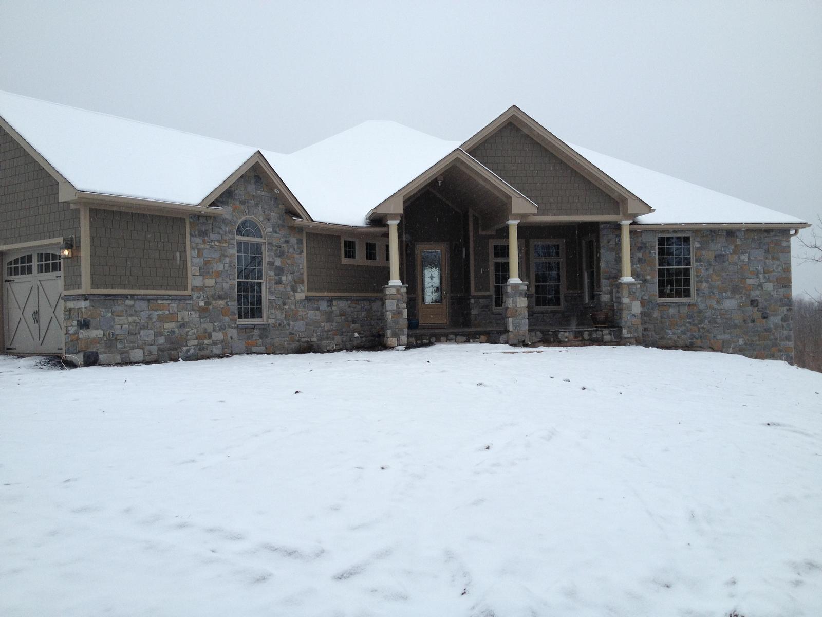 The finished house across snow, entry gable centered between the garage wing and the stone end