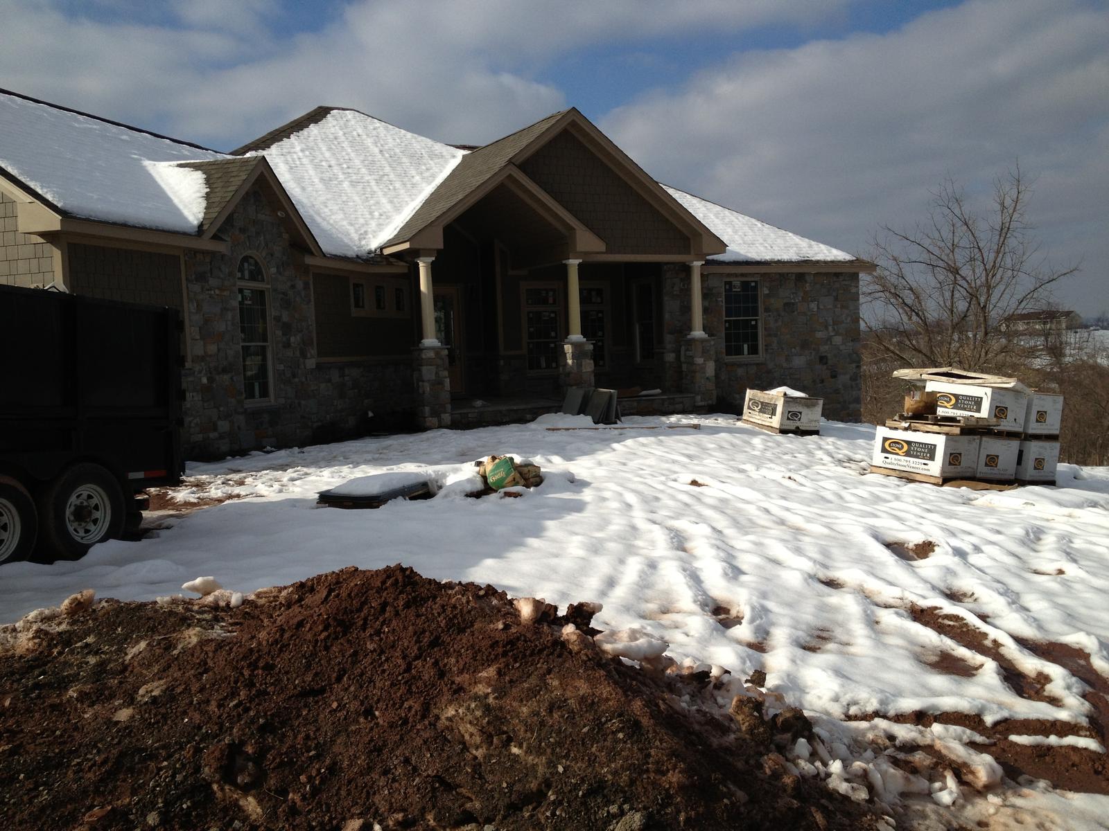 The house from the drive with snow on the ground and roof, packaged fixtures stacked outside the porch
