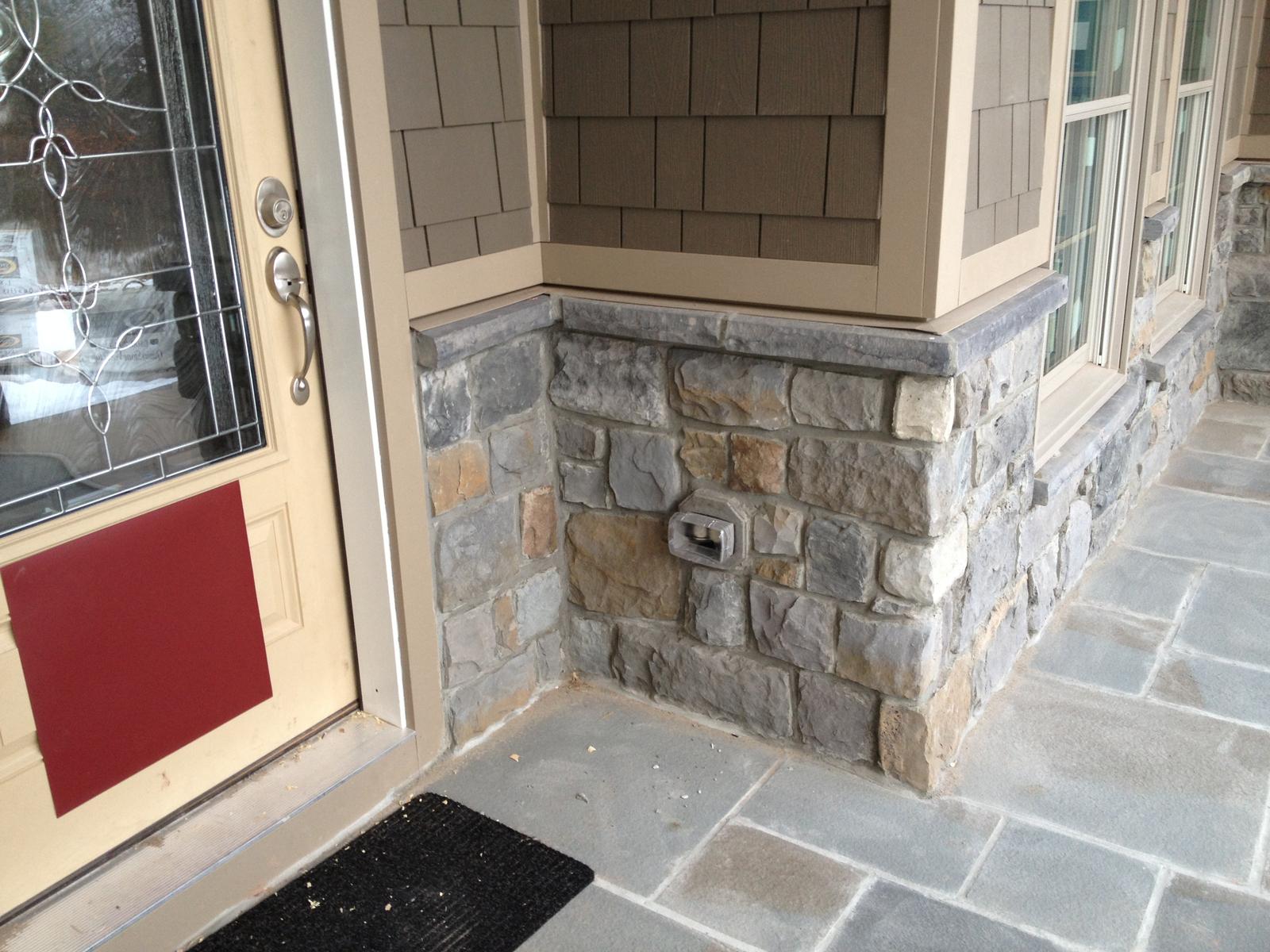 The front door and sidelight from the porch, stone wall and flagstone running away to the corner