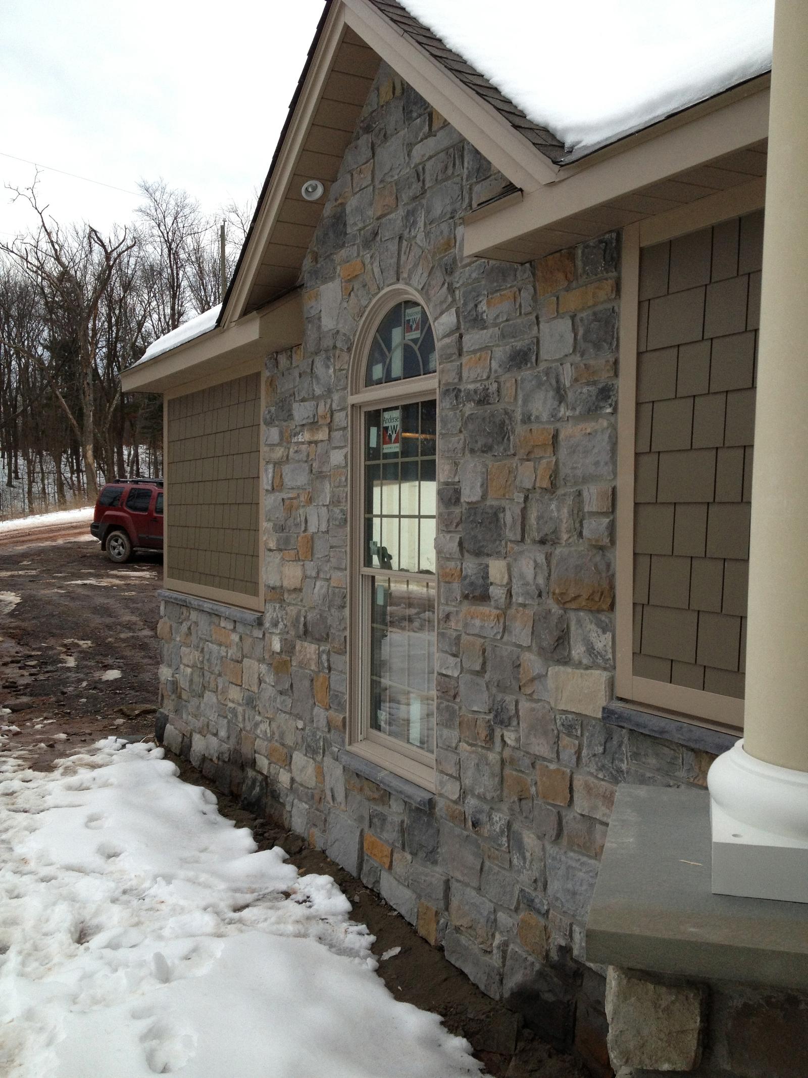 The gable end with an arched window, stone below and shingle above, snow lying against the wall