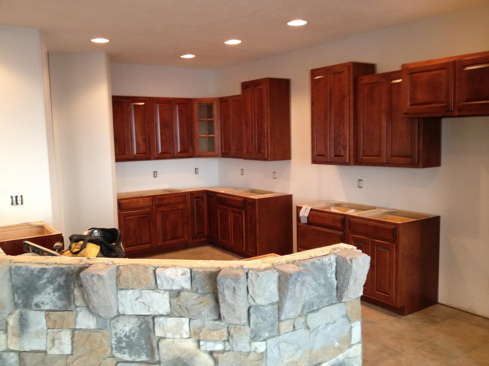 A kitchen with dark cabinets fitted and a stone-faced bar in front, counters not yet set