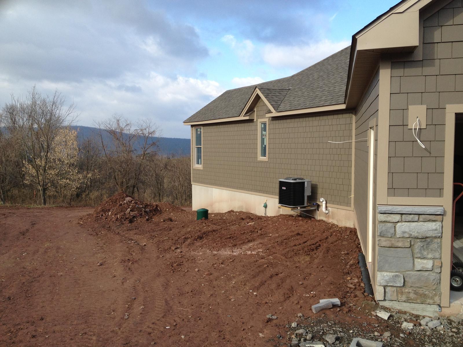 The gable end and garage wing, a mound of subsoil pushed up against the wall and a heat pump on its pad