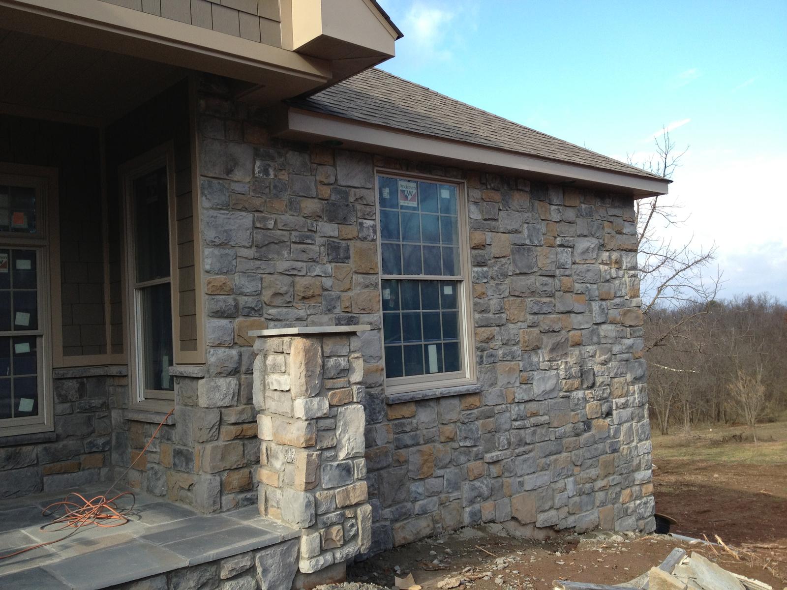 A stone corner of the house with a tall window above, the eaves and gutter finished