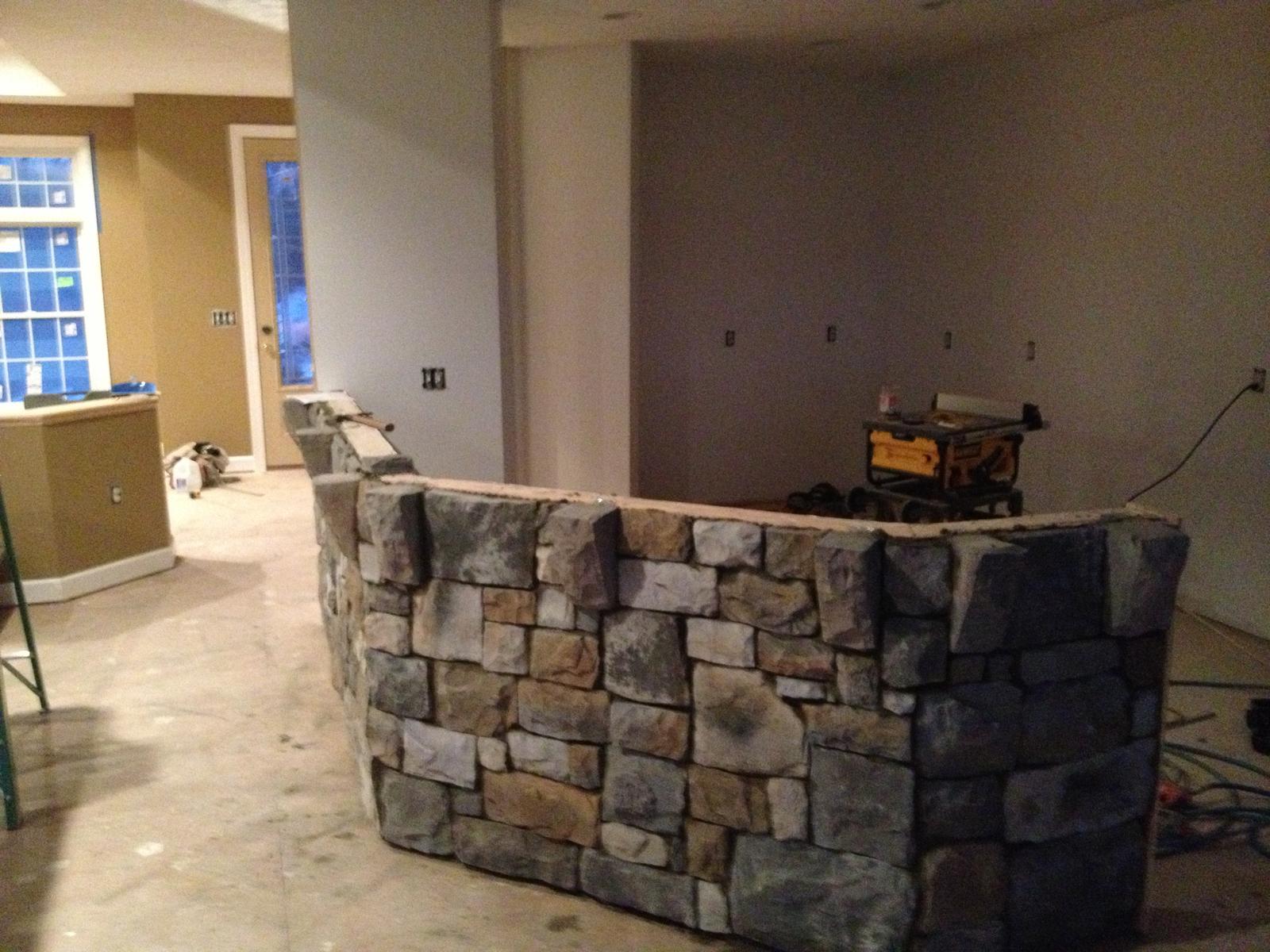 A curved stone knee-wall dividing the great room from the kitchen, still under construction