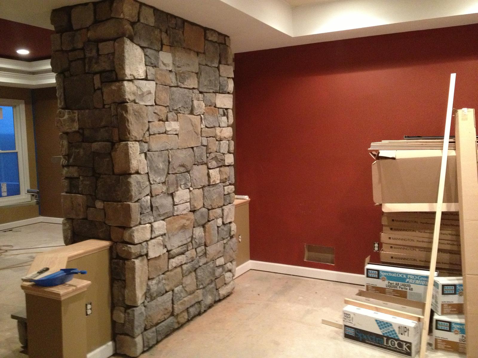 A stone column built floor to ceiling beside a deep red wall, flooring cartons stacked ready on the floor
